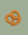 An orange-brown dog chew toy shaped like a pretzel, shown on a solid sage green background. The brand name 'Peanut' is embossed on the center.