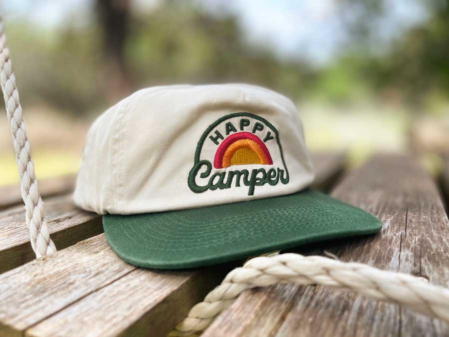 Cap with 'Happy Camper' logo on a wooden surface outdoors