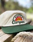 Cap with 'Happy Camper' logo on a wooden surface outdoors