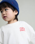 A young child wearing a blue knit beanie and a white sweatshirt with red 'FISH & CHIPS' text on the chest, photographed against a plain light gray background.