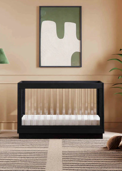 Modern black crib in a stylish room with abstract art, lamp, and plant.