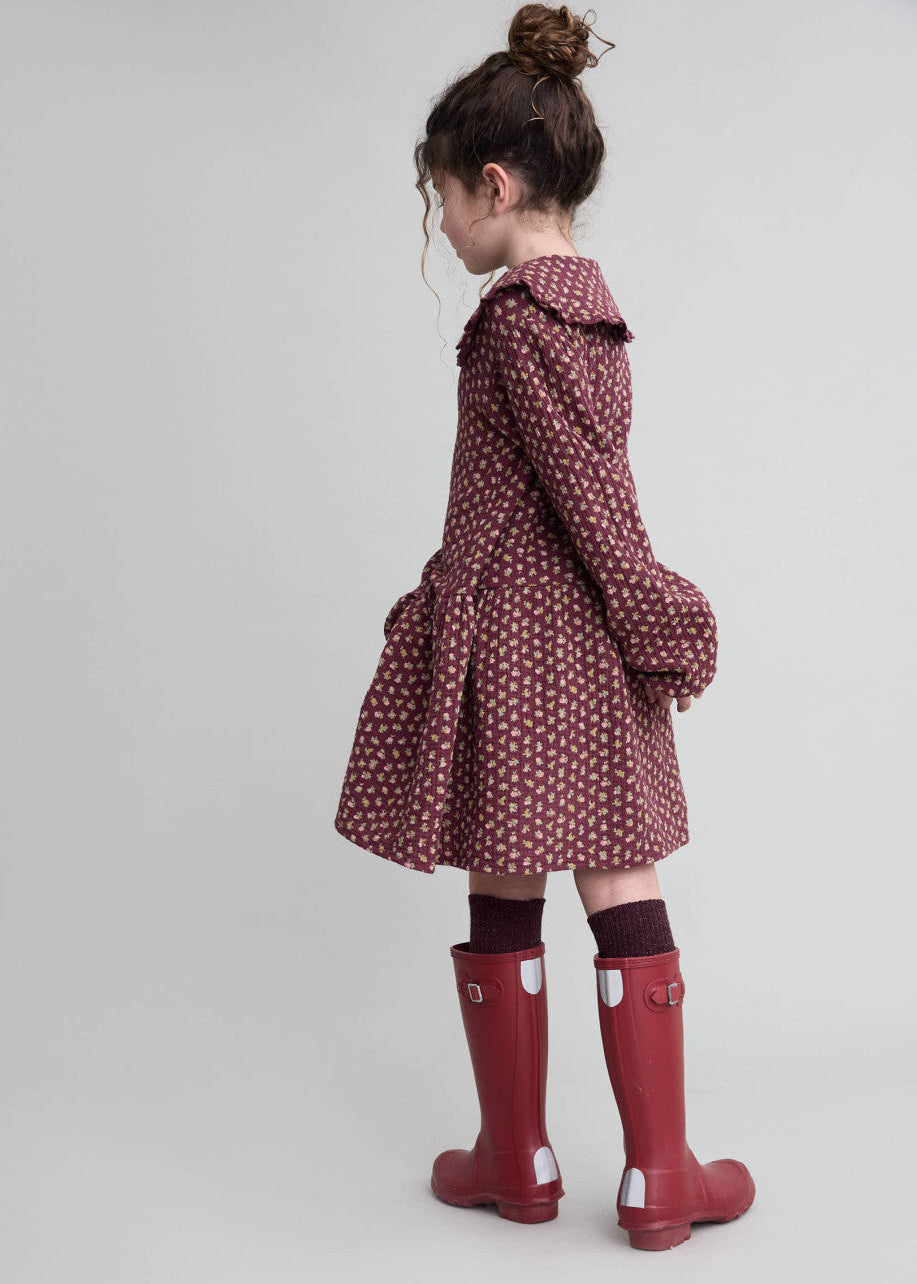 Child wearing a patterned coat and red rain boots on a plain background