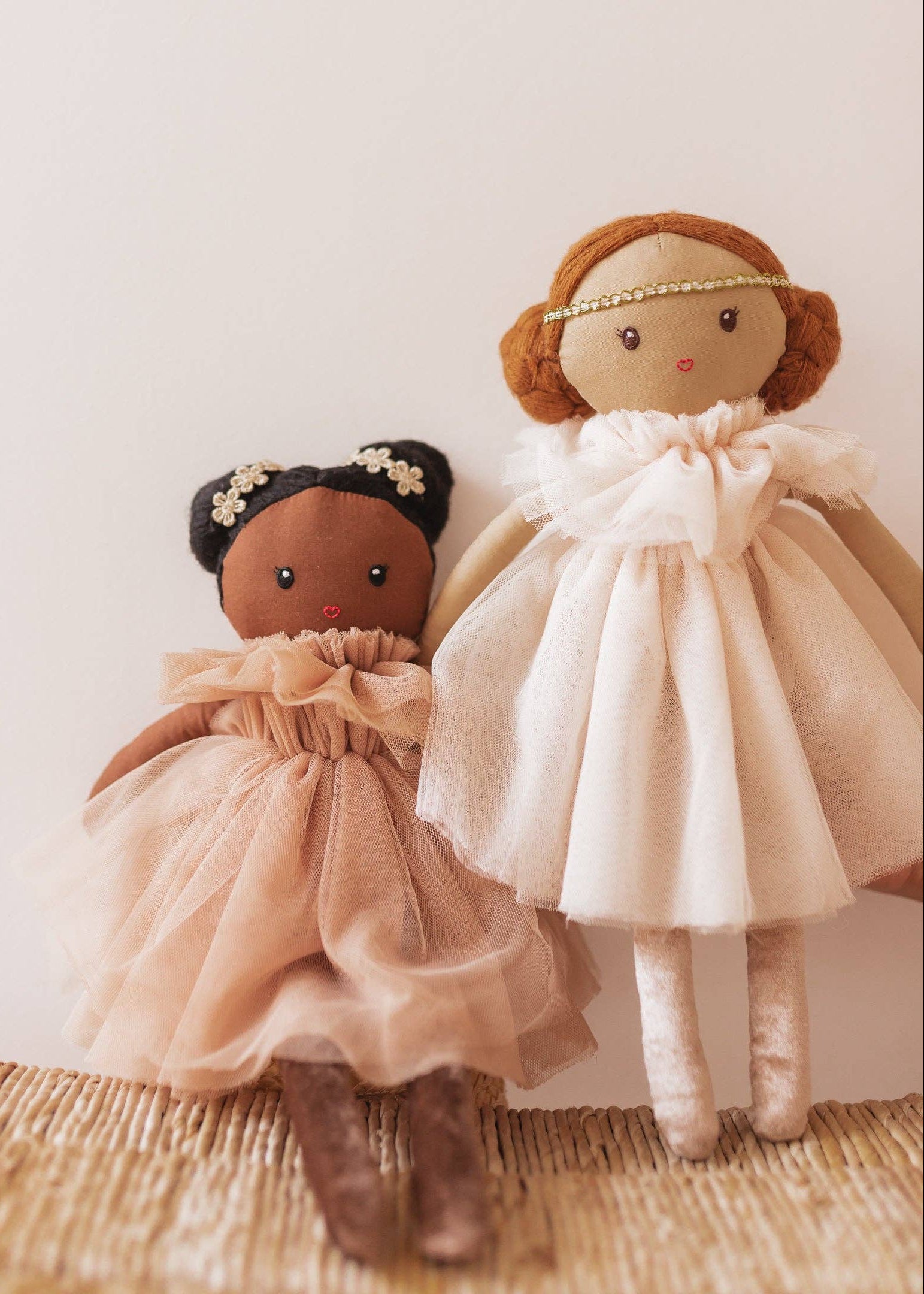 Two dolls in dresses on a textured surface with a neutral background