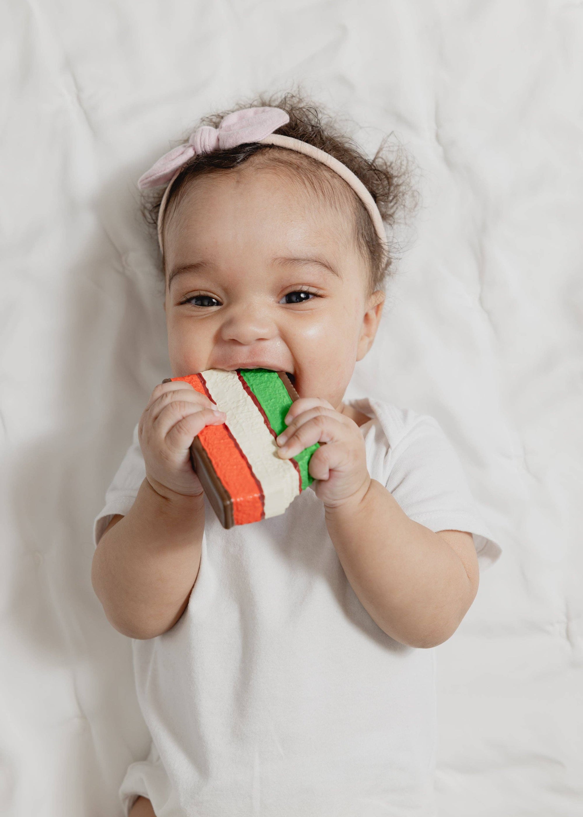 Baby lying on a white blanket with a colorful teething toy.