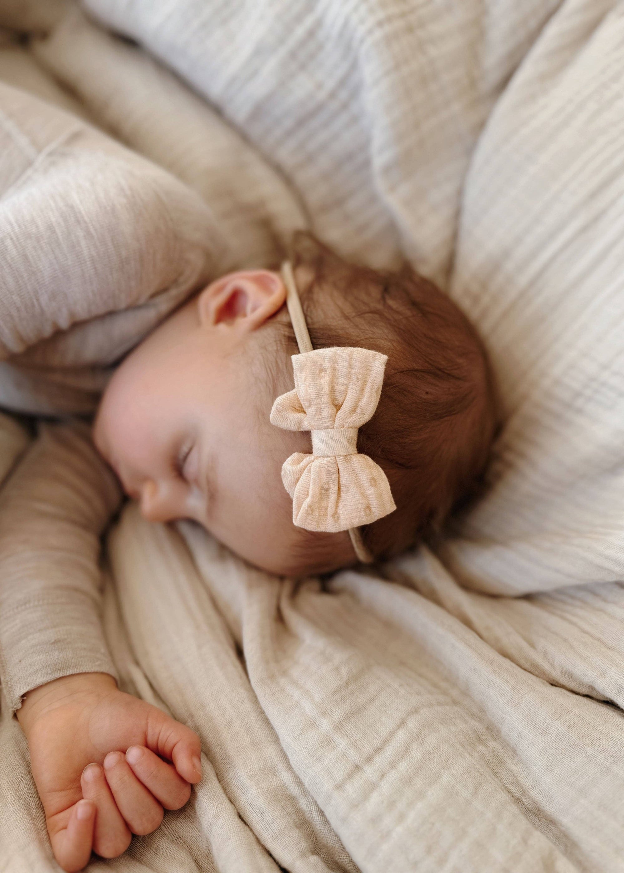 Baby sleeping with a bow headband on a soft beige blanket