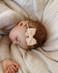 Baby sleeping with a bow headband on a soft beige blanket