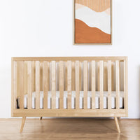 Nursery room with wooden crib and dresser, abstract art on the wall.