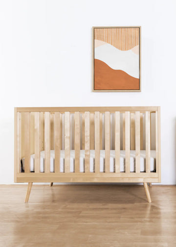 Nursery room with wooden crib and dresser, abstract art on the wall.