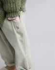 Light-colored pants with a small red logo worn by a person in a green textured sweater on a light gray background