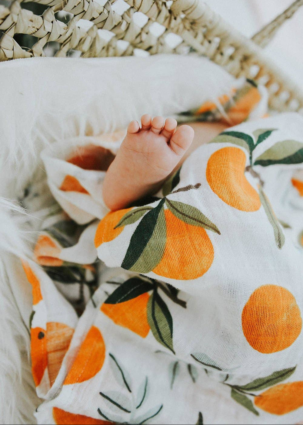 Baby wrapped in a blanket with orange and green pattern, lying on a textured surface.