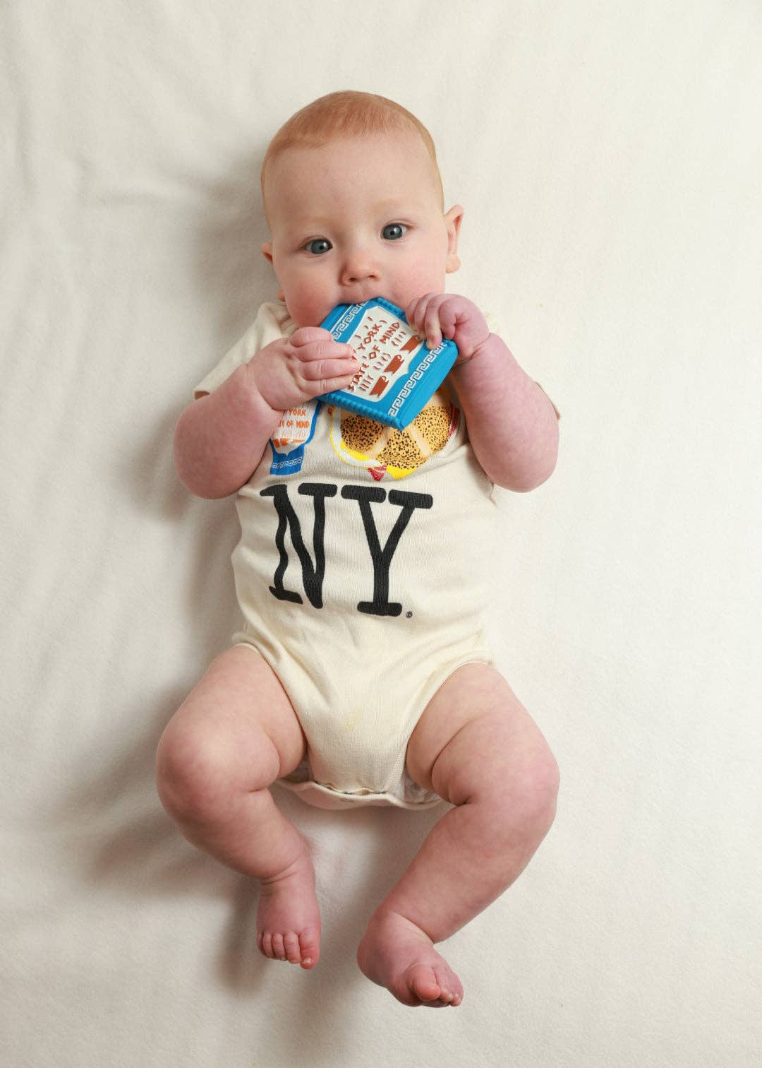Baby wearing a onesie with 'NY' holding a toy on a white background