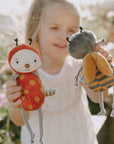 Child holding two plush toys resembling a ladybug and a bee outdoors.