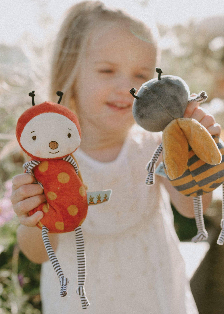 Child holding two plush toys resembling a ladybug and a bee outdoors.