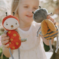 Child holding two plush toys resembling a ladybug and a bee outdoors.