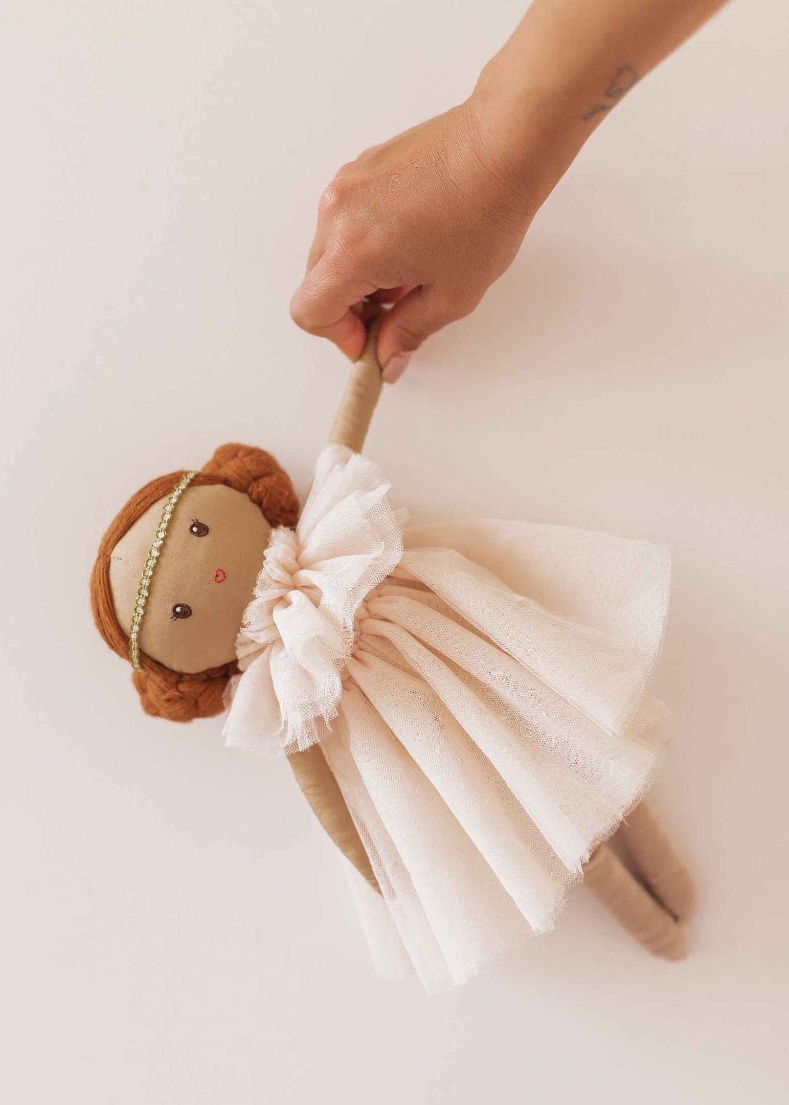 Hand holding a plush toy lion with a white tulle skirt on a light background