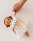 Hand holding a plush toy lion with a white tulle skirt on a light background