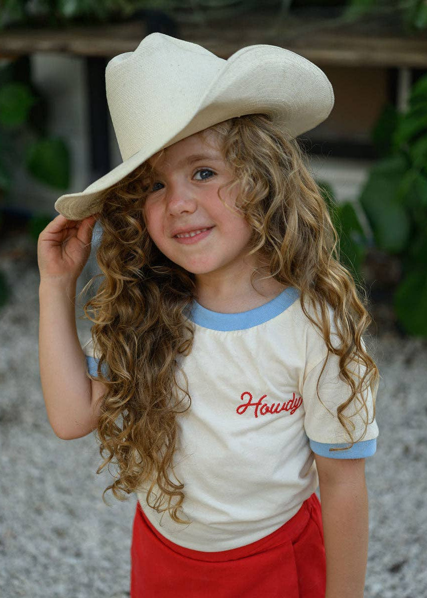 Child wearing a cowboy hat and 'Howdy' shirt outdoors