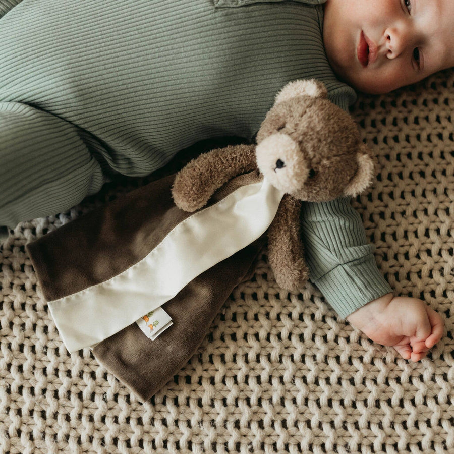 Baby lying on a textured surface with a brown teddy bear toy