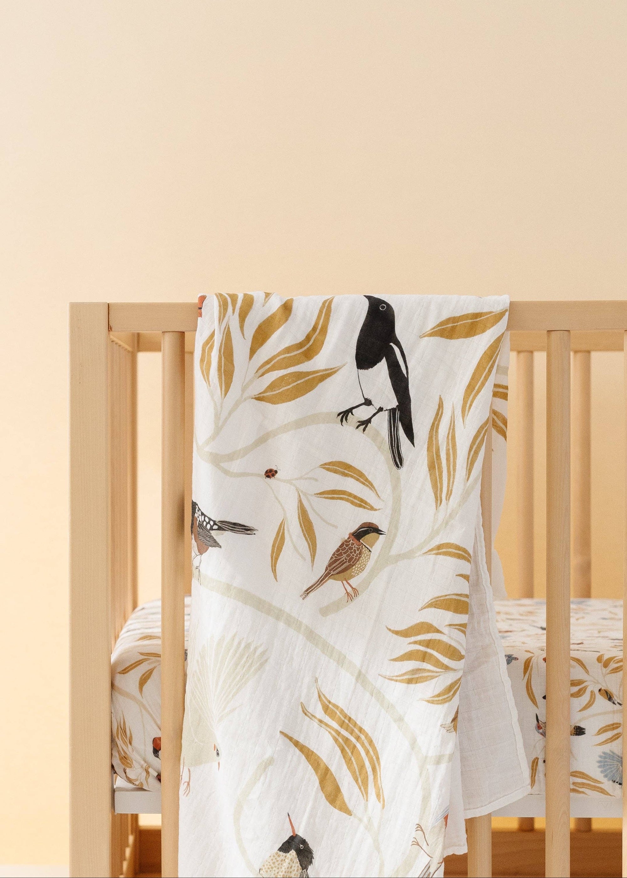 Crib with a white blanket featuring bird and leaf patterns on a beige background