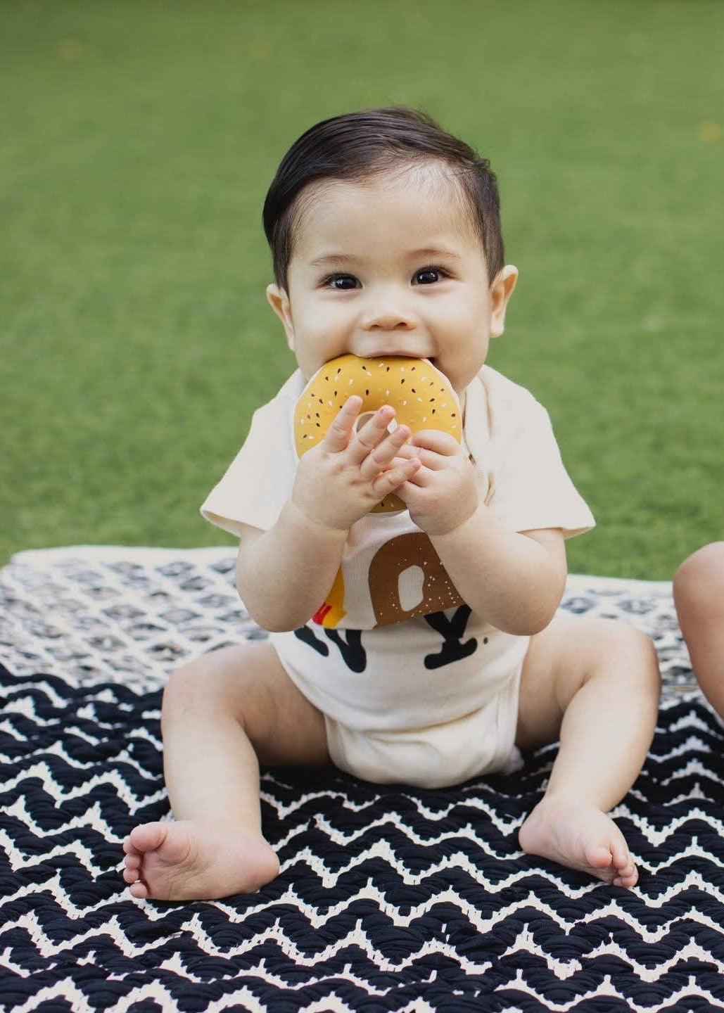 Two babies sitting on a black and white chevron blanket on green grass, wearing matching white t-shirts with food graphics.