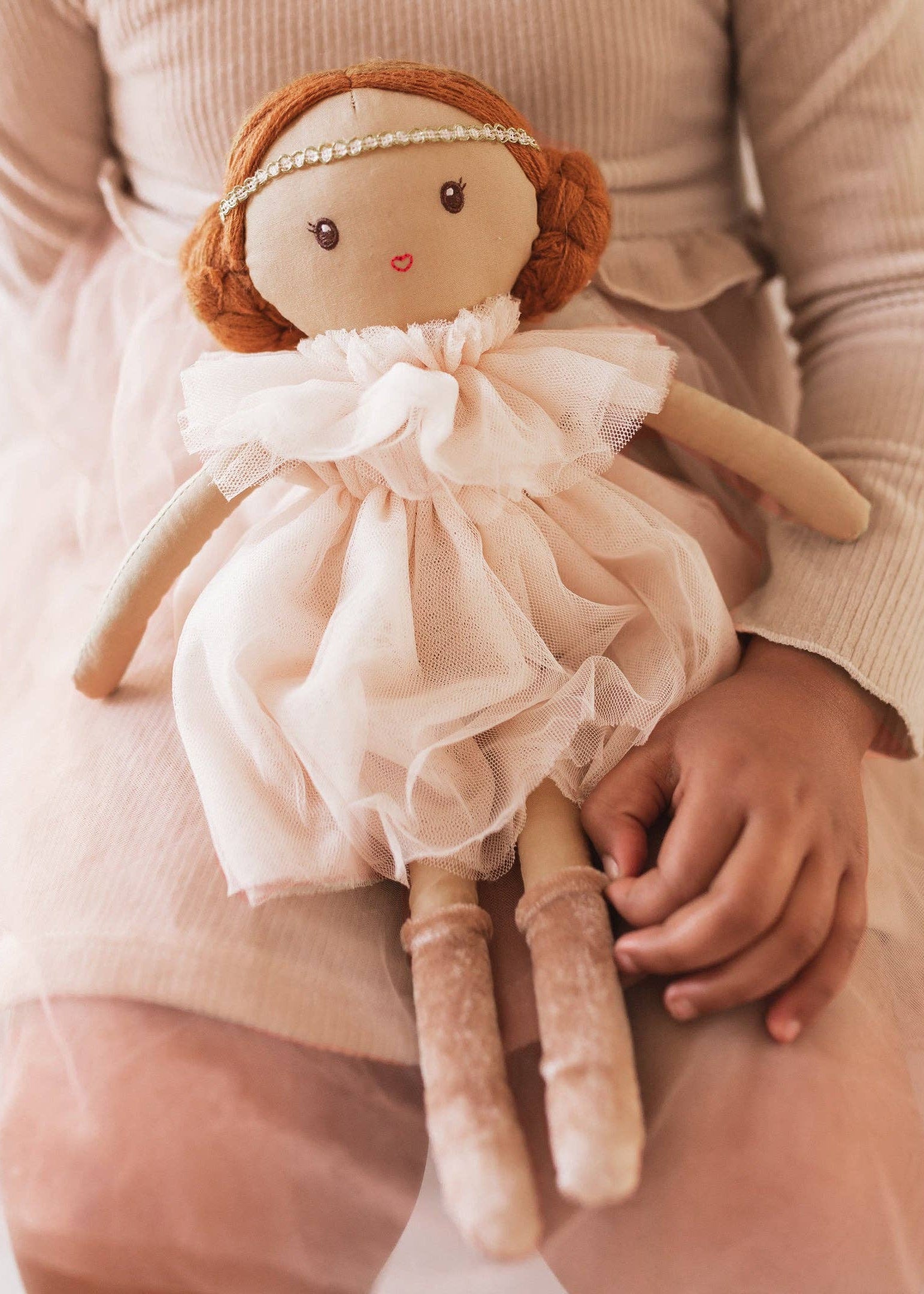 Hand holding a small doll with a delicate dress and red hair.
