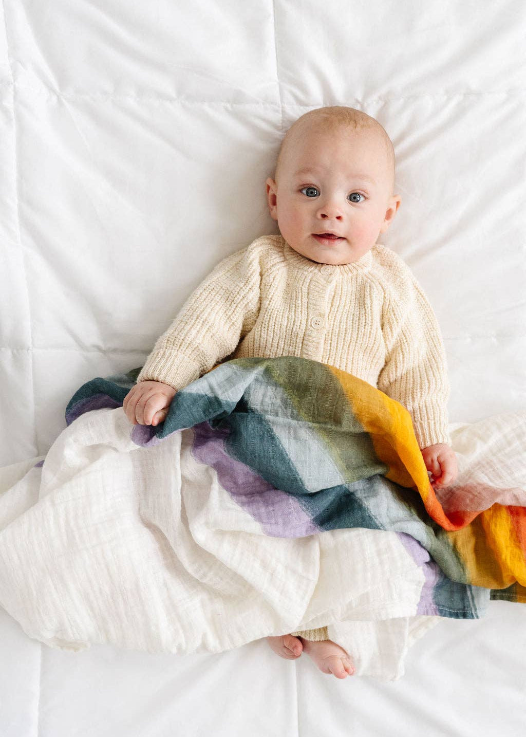 Baby lying on a white blanket with a colorful striped blanket