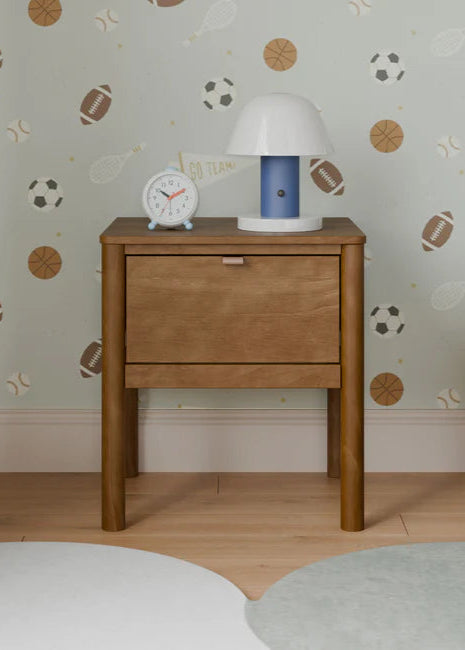 Wooden nightstand with lamp and clock against a wall with sports-themed wallpaper