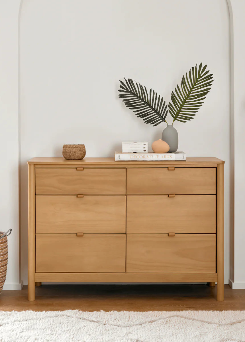 Wooden dresser with decorative items in a room with a white wall and lamp.