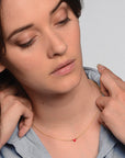 Woman wearing a gold necklace with a red heart pendant, with hands gently touching her shoulders.