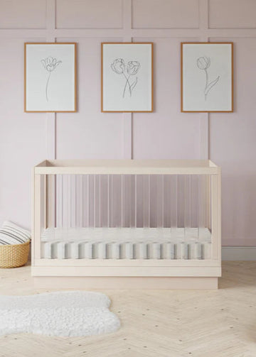 Wooden crib in a room with light pink walls, framed artwork, and decorative items.