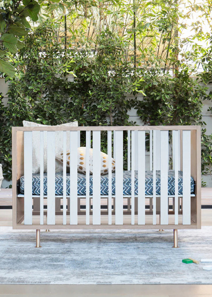 Wooden crib in a nursery with greenery and a rug