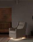 Modern nursery with a beige armchair, wooden crib, and decorative wall piece.