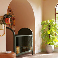 Modern nursery with a green crib, plant, and dresser.