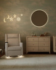 Nursery room with a crib, dresser, and armchair against a cloud-patterned wall.