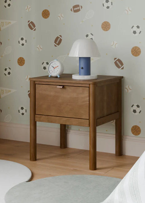 Wooden nightstand with lamp and clock against a wall with sports-themed wallpaper