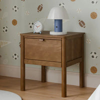 Wooden nightstand with lamp and clock against a wall with sports-themed wallpaper