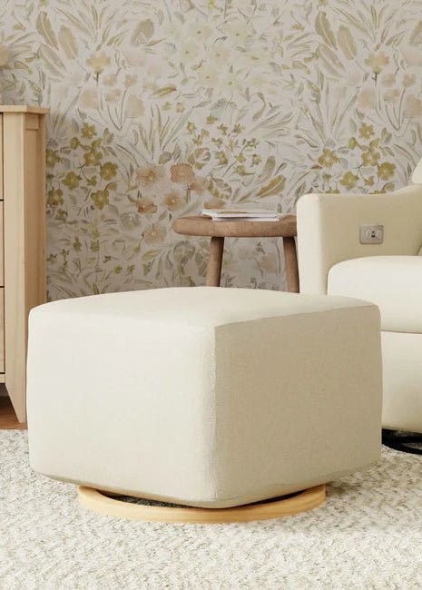 Beige ottoman in a living room with floral wallpaper and a beige armchair.