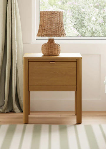 Wooden nightstand with a lamp next to a bed in a bedroom.