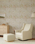 Living room with cream armchair, ottoman, and dresser against a floral wallpapered wall.