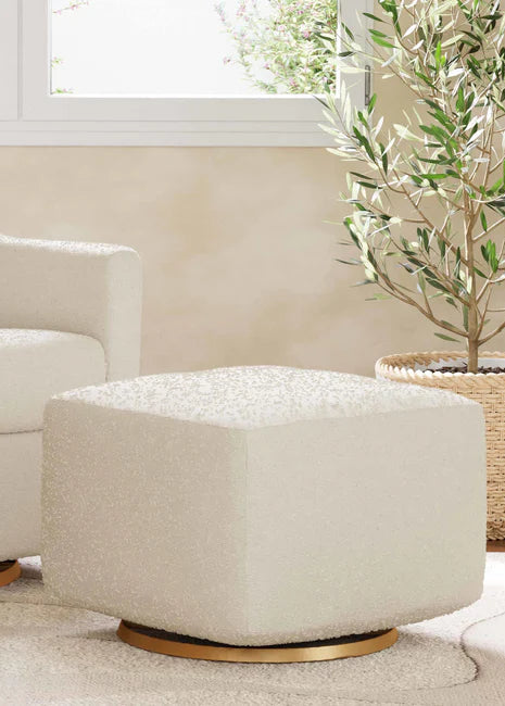 Beige armchair and ottoman with gold bases in a room with a window and plant.