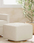 Beige armchair and ottoman with gold bases in a room with a window and plant.