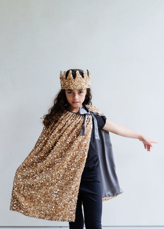 Person wearing a gold sequin cape and crown against a plain background