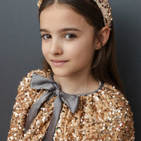 Young girl wearing a gold sequin outfit with a matching headband against a dark background