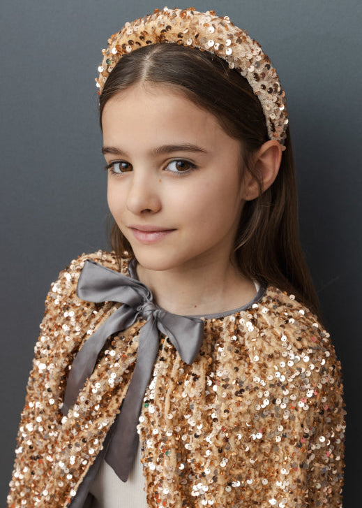 Young girl wearing a gold sequin outfit with a matching headband against a dark background