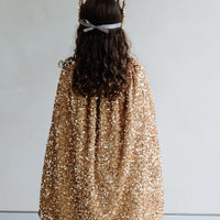 Person wearing a gold sequin cape from behind on a plain background