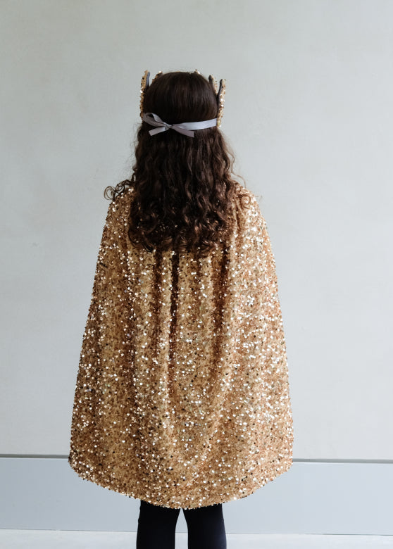 Person wearing a gold sequin cape from behind on a plain background
