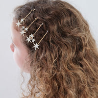Person with curly hair wearing gold star-shaped hair accessories on a plain background