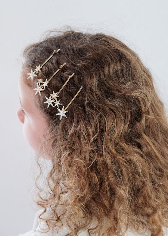 Person with curly hair wearing gold star-shaped hair accessories on a plain background
