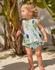 Child wearing a floral dress standing outdoors with plants in the background