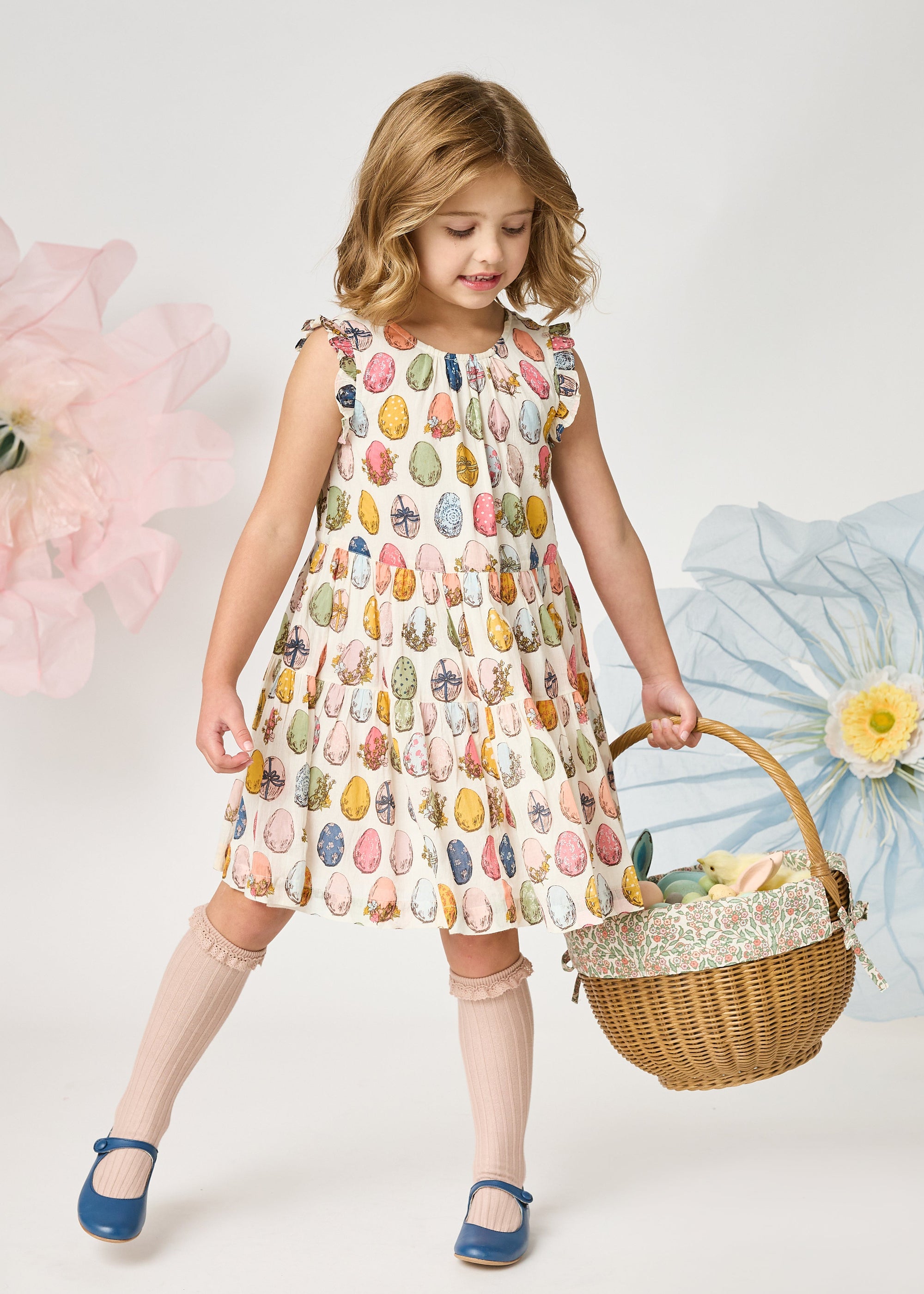 Young girl in a patterned dress holding a basket with flowers against a white background